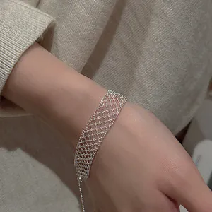 Detail of silver hollow mesh grid bracelet worn on wrist with beige sweater