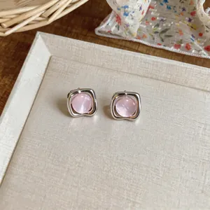 Dettaglio di orecchini a lobo rosa con montatura quadrata argentata su espositore.