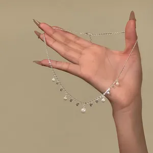 Close-up view of a silver necklace with dangling pearls and zircons on a hand.