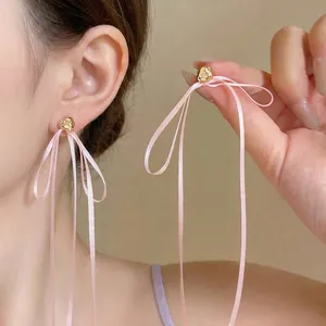 Élégantes boucles d'oreilles cœur doré avec de longs rubans roses portées par un mannequin