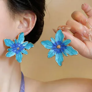 Detailed view of vibrant blue enamel flower stud earrings with gold trim worn on ear.
