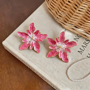 Close-up of elegant pink and white enamel flower stud earrings with gold-toned edges.