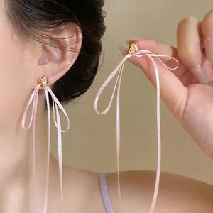 Détail de boucles d'oreilles élégantes à nœud rose et accents dorés sur un mannequin asiatique