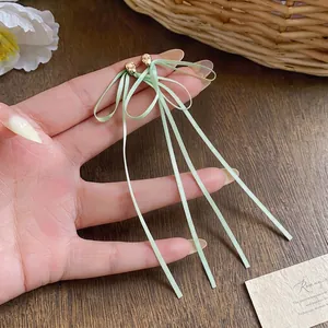 Gros plan de boucles d'oreilles nœud en ruban vert pâle avec de longs glands.