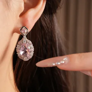 Dettaglio di eleganti orecchini pendenti con zircone rosa, indossati con stile chic.