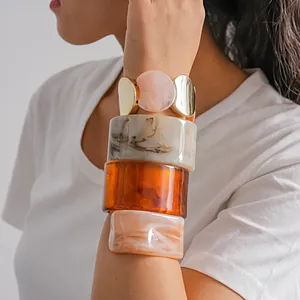 Détail de quatre joncs en acrylique marbré et d'un bracelet doré sur le poignet d'un mannequin