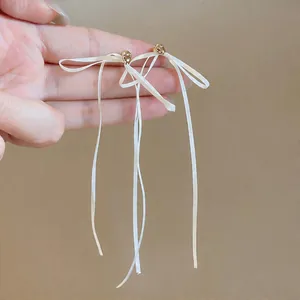 Vue détaillée de longues boucles d'oreilles en ruban blanc avec des accents dorés.