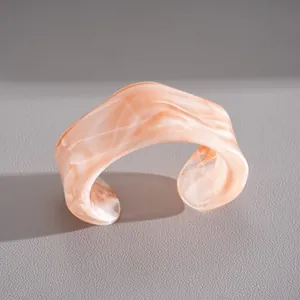 Gros plan d'un bracelet manchette en acrylique marbré pêche avec texture résine