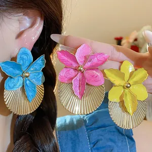 Primo piano di orecchini a fiore in smalto colorato con dischi in metallo dorato plissettato chic