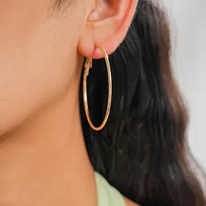 Detail view of a model wearing large minimalist gold hoop earrings with a polished finish