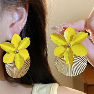 Dettaglio di orecchini a fiore giallo con accenti rotondi plissettati dorati.