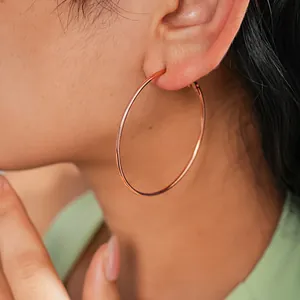 Close-up view of a minimalist large rose gold hoop earring worn by a female model