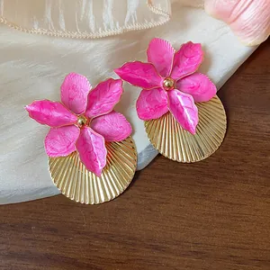 Vista dettagliata di orecchini a fiore in smalto rosa con base a disco oro pieghettato