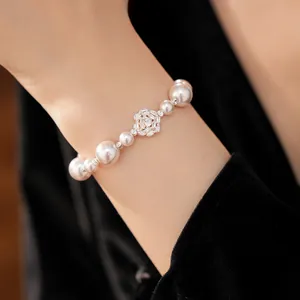 Close-up of elegant pearl bracelet featuring a zircon-studded flower charm on a wrist