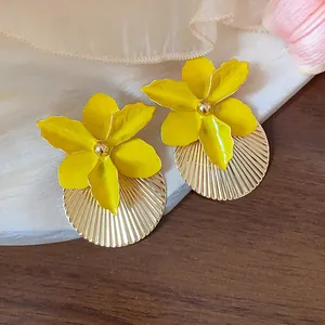 Primo piano di orecchini a fiore giallo smaltato con base circolare a pieghe dorate