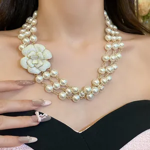 Close-up detail of a triple-layer pearl necklace with a white enamel camellia flower.