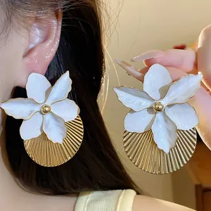 Primo piano dei dettagli degli orecchini a fiore bianco smaltato con disco plissé dorato chic.