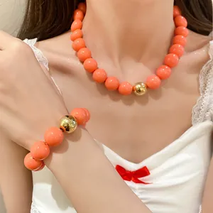 Close-up detail of orange chunky bead necklace and bracelet set with gold accent.