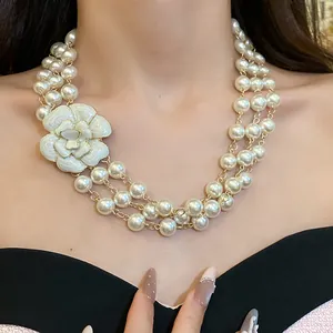 Detail of multi-layer glass pearl necklace with elegant white enamel camellia flower.