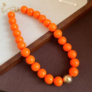 Close-up of vibrant orange chunky beads and gold sphere detail on fashion necklace.