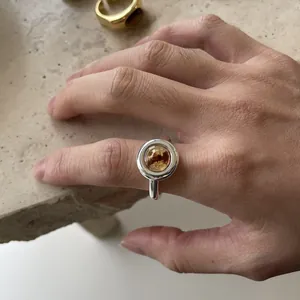 Detailed view of a Maillard-style silver open ring with a circular amber resin centerpiece