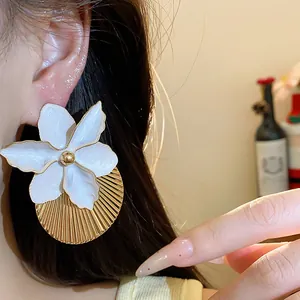 Dettaglio macro di un elegante orecchino a fiore bianco con un disco d'oro a pieghe.