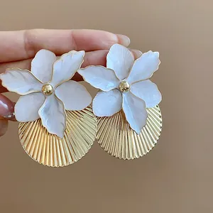 Dettaglio di orecchini a fiore in smalto bianco con base a disco plissettato in oro
