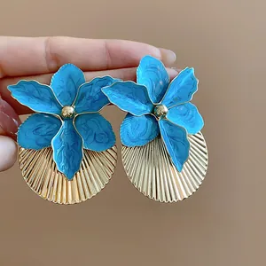 Dettaglio orecchini a fiore in smalto blu con grandi dischi dorati a pieghe sole.