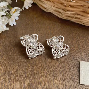 Detalle de pendientes de botón con flores caladas de plata y piedras de circonita