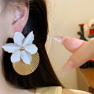 Primo piano di un elegante orecchino a fiore in smalto bianco con base rotonda plissettata d'oro.