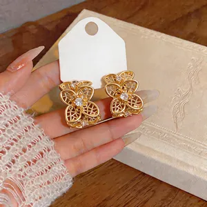 Detalle de pendientes de flores huecas doradas en forma de C con circonitas brillantes