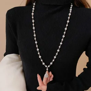 Close-up of long imitation pearl necklace with baroque pendant on black turtleneck