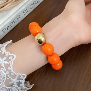 Close-up of a bold orange beaded bracelet with a large gold bead on a woman's wrist
