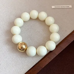 Close-up of oversized cream beads and a single gold bead on a minimalist bracelet