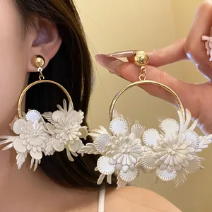 Dettaglio di eleganti orecchini a cerchio con fiori in ecopelle bianca e finitura oro