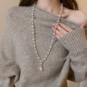 Elegant model wearing vintage Baroque irregular pearl pendant necklace on beige sweater.