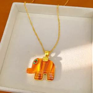 Close-up of a bohemian orange resin elephant pendant on a delicate gold chain necklace