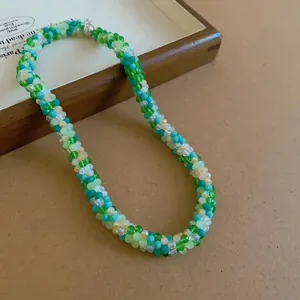 Macro detail view of a handmade woven crystal beaded necklace featuring green and blue tones