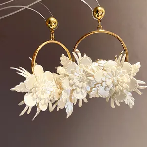 Dettaglio di eleganti orecchini a cerchio dorati con fiori in pelle bianca e perle.