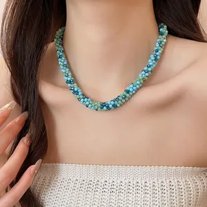 Close-up of a woven beaded crystal necklace in blue and green tones worn by a model.