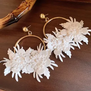 Dettaglio ravvicinato di eleganti orecchini a cerchio con fiori in pelle bianca e perno d'oro