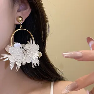 Dettaglio di orecchini a cerchio con fiori in pelle bianca e finitura color oro