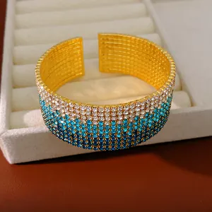 Primo piano di un bracciale a fascia dorato a più file con strass sfumati blu e bianchi.