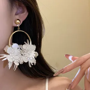 Dettaglio ravvicinato di eleganti orecchini a cerchio con fiori in pelle bianca su modella