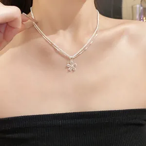 Detail of double-layer silver-toned necklace with sparkling flower zircon pendant on model.