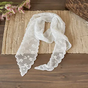 Close-up detail of a white floral lace skinny scarf presented on a rustic woven mat.