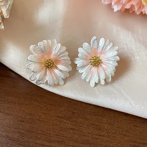 Vista dettagliata di orecchini a margherita in smalto bianco con petali glitterati e oro