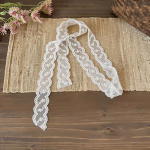 Elegant white floral lace ribbon scarf displayed on a rustic straw mat with flowers