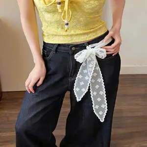 Close-up of white floral lace ribbon scarf used as a decorative belt on denim jeans