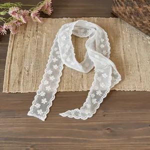 Close-up of white floral lace skinny scarf with scalloped edges on a rustic mat.